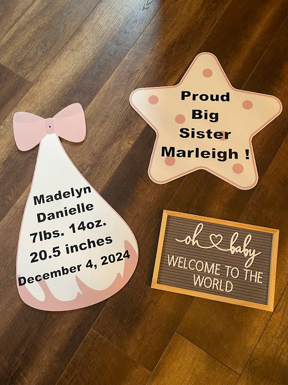 Decorative signs for a new baby on a wooden floor, including a star-shaped sign and a baby dress-shaped sign.